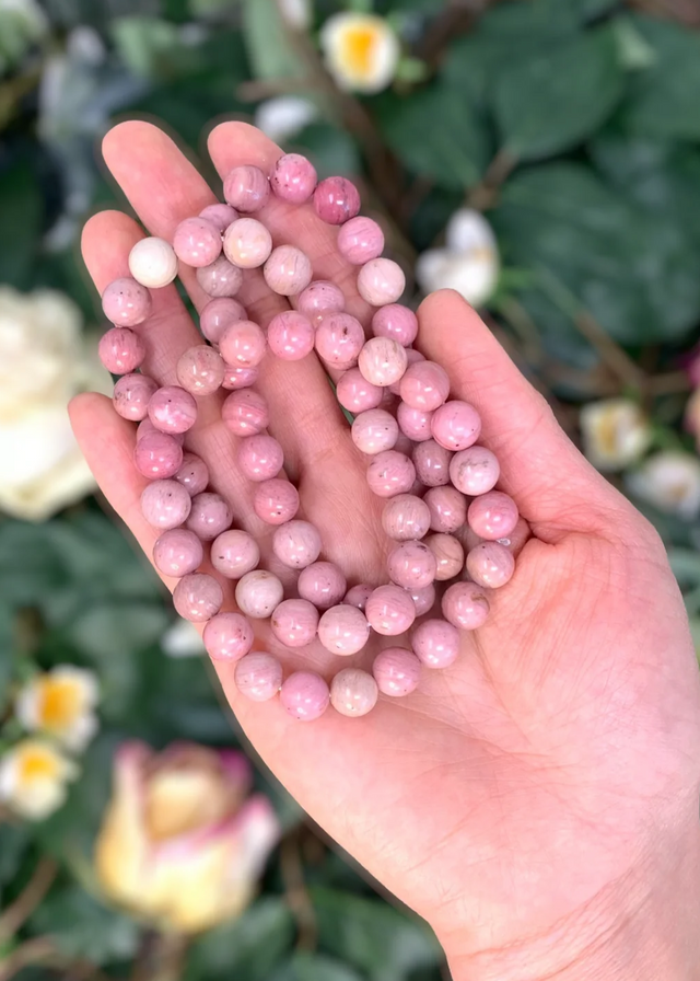 Hand holding pink beads with a blurred natural background